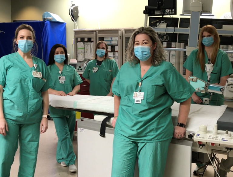 Nurses in scrubs and masks around an operating table