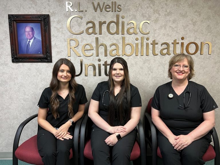 3 women sitting infront of a sign
